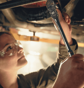 Female mechanic working under a vehicle that is up on a lift