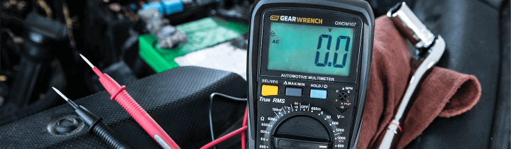 GEARWRENCH digital multimeter with an open engine bay behind it