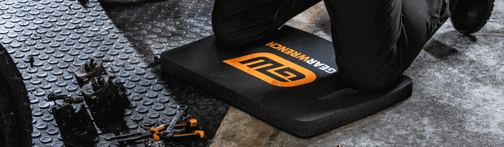 Male mechanic kneeling on a GEARWRENCH kneeling mat working on a car