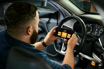 Male auto technician looking at the GWSMARTBT app on his phone diagnosing issues with a car while sitting in it