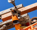 Utility worker in an aerial bucket using a GEARWRENCH ratcheting wrench to fasten hardware on a wooden utility pole crossarm.
